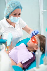 Pediatric dentist protecting female child eyes before dental procedure