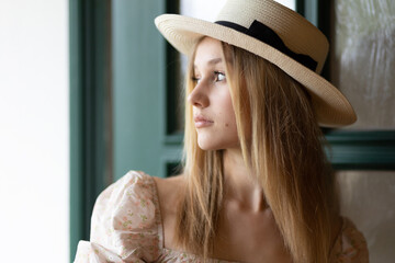 A young girl in a straw hat stands near the front door and looks back.