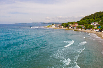 Sandy coast, buildings and blue sea with waves. San Juan, La Union, Philippines. The beaches of the Philippine Islands. Town near the sea.