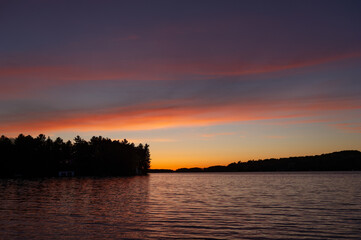 Naklejka premium Beautiful sunset on a calm lake in Muskoka, in the sky the orange hues are visible.