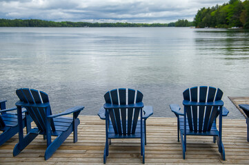 Blue Adirondack chairs on a wooden dock facing a lake in Muskoka, Ontario.