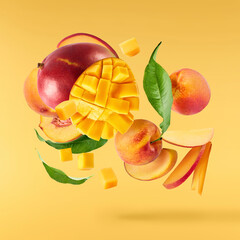 Fresh ripe whole and sliced mango and peaches with green leaves falling in the