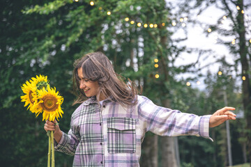 A young woman with a bouquet of sunflowers on a blurred background in nature.