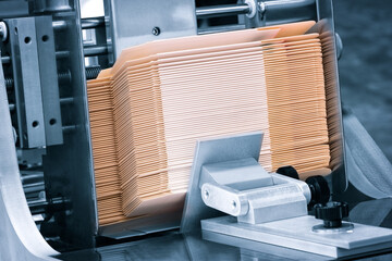 Elements of corton boxes are collected in stack. Conveyor line for the production of boxes. Machine cuts cardboard boxes from sheets of cardboard. Enterprise for the production package.