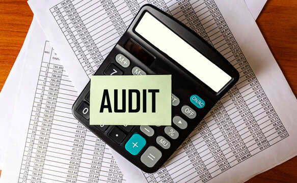 The word AUDIT is written on a sticker that lies on a calculator and documents with calculations.. Close-up