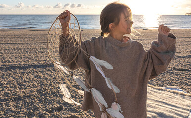 Little girl with a dream catcher on the seashore at sunset.