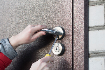 Handyman checks door lock in front metallic door. Checking lock for operability.