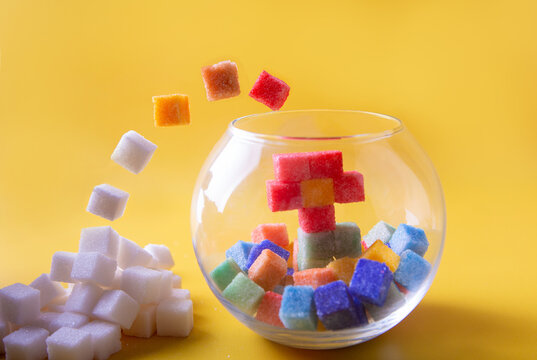 White sugarcubes jumping into glass aquarium and become colorful. Pile of white sugar cubes, red, green flower, yellow background