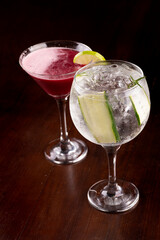mixology two cocktail glasses with martini, berries, gin, cucumber, rosemary, ice on wooden table