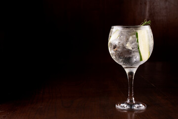 mixology two glasses of gin tonic cocktail, with rosemary and cucumber and lots of ice under wooden...