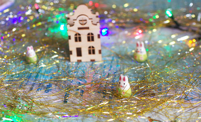 Closeup of three cute little rabbits with a miniature wooden house. A symbol of new year 2023 with a tinsel and a colorful garland. Christmas decorations, winter holidays concept background