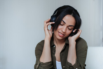 Close up African american young woman in headphones toothy smiling holding headset with eyes closed. Brazilian woman enjoying music at home. Relaxing female student. Call center employee at break.