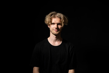 Young smiling man in a black t-shirt over black background.