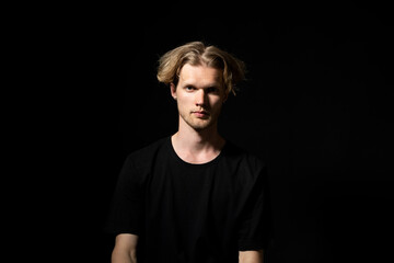 Portrait of calm serious mature young man without emotions. Beautiful emotionless guy in a black t-shirt looking to the camera, isolated over black background.