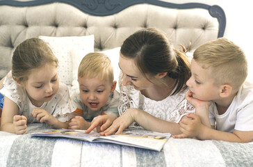 Children lie on the bed in the bedroom, mother reads a book to them.