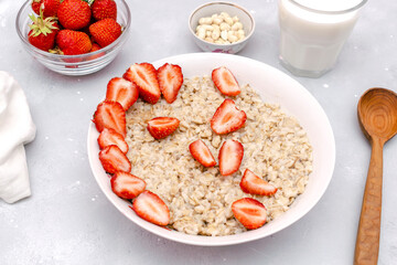 Oatmeal porridge with summer strawberries berries. Porridge oats in bowl with milk,nuts. Healthy food breakfast,lifestyle,dieting, proper nutrition. Top view flat lay on gray table background