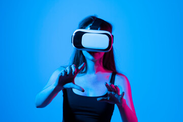 Young brunette woman in black t-shirt wearing a VR headset and looking up while playing a game with a friends in a metaverse. Virtual reality concept.