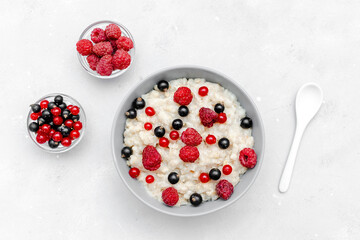Oatmeal porridge with summer raspberry, currant berries. Porridge oats in bowl with fruits. Healthy food breakfast,lifestyle,dieting, proper nutrition. Top view flat lay on gray table background