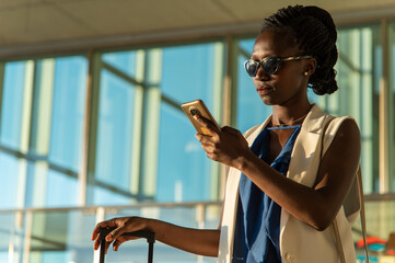  A young businesswoman using her phone standing at an airport or train station