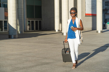 A young businesswoman traveling using her phone while carrying her suitcase