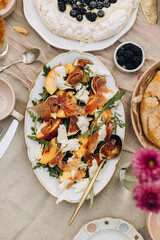 dish with sliced peaches, figs, mozzarella pieces, arugula and prosciutto slices. gourmet snacks for picnic top view
