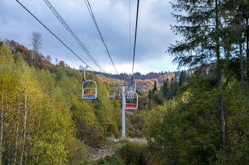 Empty aerial chair lift through colorful foliage in the autumn mountain forest 