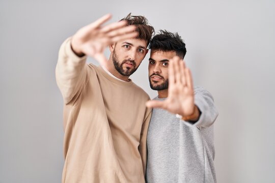 Young homosexual couple standing over white background doing frame using hands palms and fingers, camera perspective