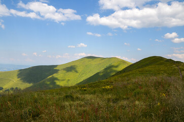 Fototapeta na wymiar Grassy green hills and slopes at ridge of Borzhava under blue sky with clouds on summer day. Carpathian Mountains, Ukraine