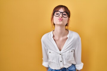 Young beautiful woman wearing casual shirt over yellow background looking at the camera blowing a kiss on air being lovely and sexy. love expression.