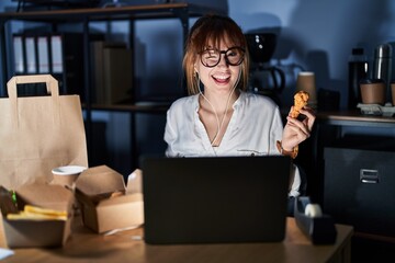 Young beautiful woman working using computer laptop and eating delivery food winking looking at the...