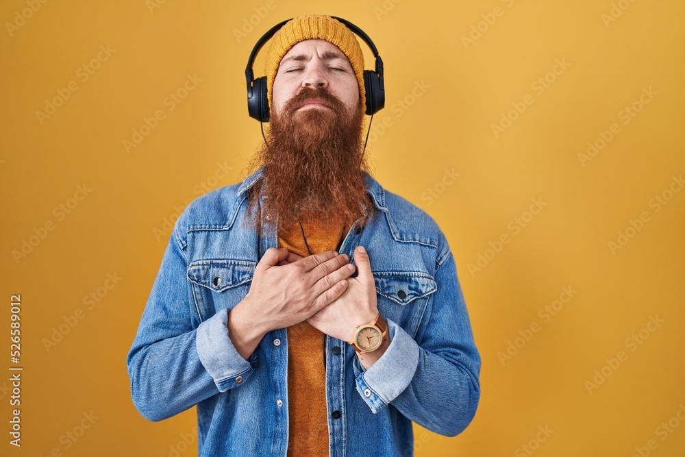 Sticker Caucasian man with long beard listening to music using headphones smiling with hands on chest with closed eyes and grateful gesture on face. health concept.