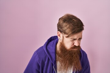 Caucasian man with long beard standing over pink background with hand on stomach because indigestion, painful illness feeling unwell. ache concept.