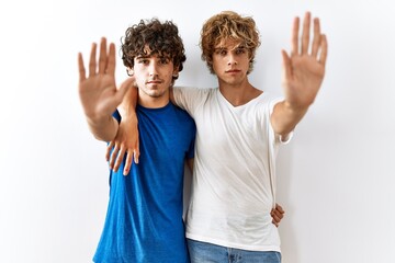 Young gay couple standing together over isolated background doing stop sing with palm of the hand. warning expression with negative and serious gesture on the face.