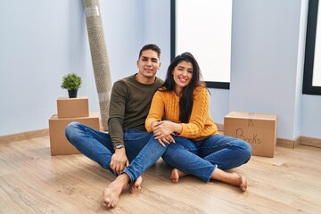 Young couple sitting on the floor at new home winking looking at the camera with sexy expression,...