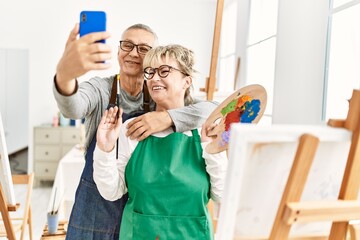 Two senior paint student smiling happy making selfie by the smartphone at art studio.