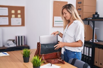 Young blonde woman business worker smiling confident holding laptop of briefcase at office