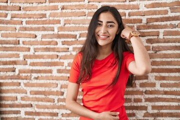 Young teenager girl standing over bricks wall smiling pointing to head with one finger, great idea or thought, good memory