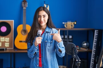 Young teenager girl singing song using microphone pointing finger to one self smiling happy and proud