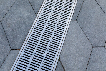 Metal storm sewer grate on shaped paving slabs in park. Drainage systems on paving slabs. Sidewalk...
