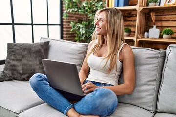 Young blonde woman using laptop sitting on sofa at home