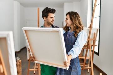 Two hispanic students smiling happy holding canvas at art school.