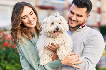 Man and woman holding dog hugging each other at park