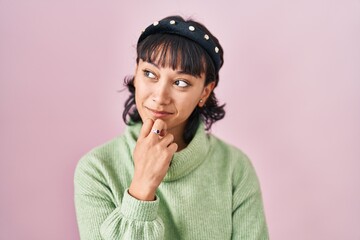 Young beautiful woman standing over pink background with hand on chin thinking about question, pensive expression. smiling with thoughtful face. doubt concept.