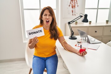 Hispanic woman supporting blood donation angry and mad screaming frustrated and furious, shouting...