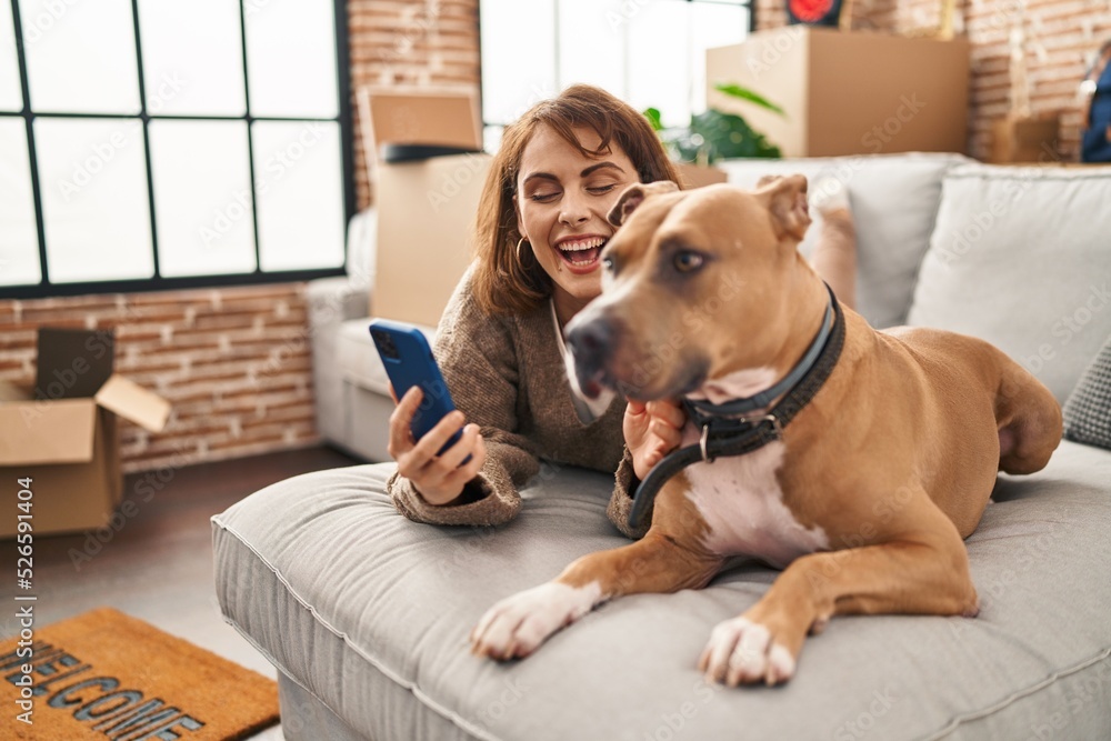 Sticker Young caucasian woman make selfie by the smartphone lying on sofa with dog at new home