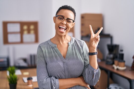 African american woman working at the office wearing glasses smiling with happy face winking at the camera doing victory sign. number two.
