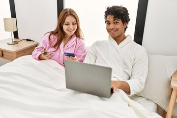 Young couple smiling happy using laptop, smartphone and credit card at bedroom.