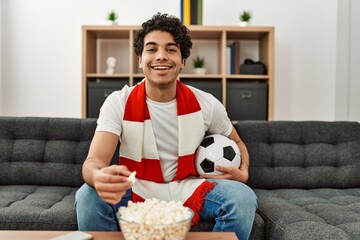 Young hispanic man watching soccer match and supporting team at home.