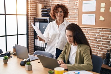 Two women business workers using laptop reading document at office