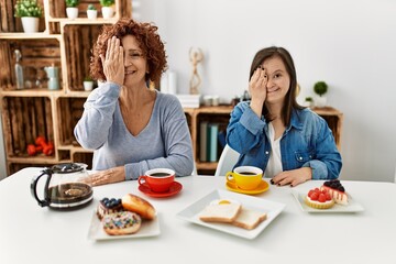 Family of mother and down syndrome daughter sitting at home eating breakfast covering one eye with hand, confident smile on face and surprise emotion.